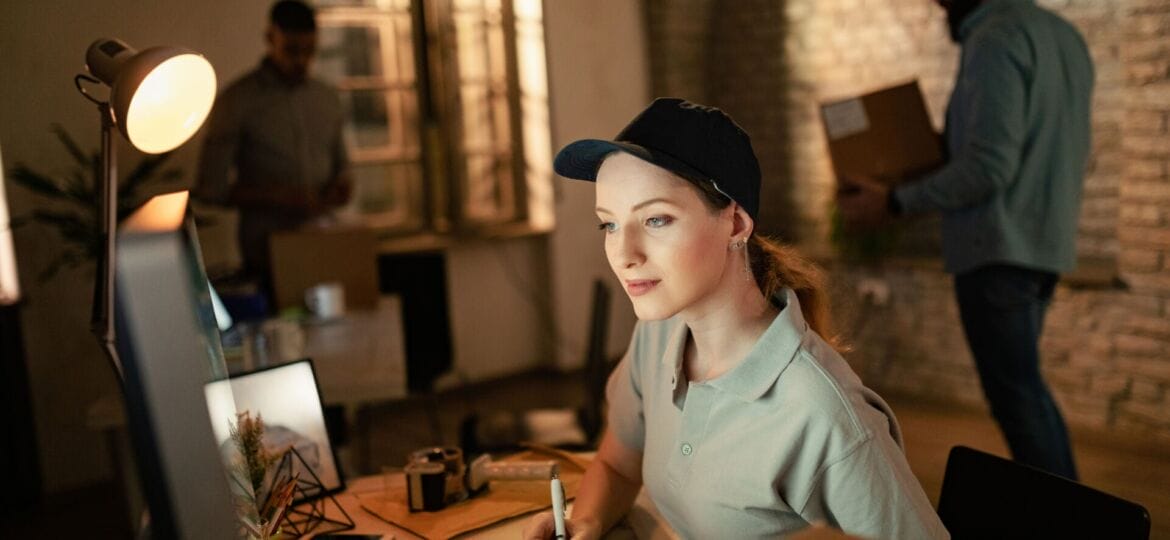 Female courier using computer while preparing package for a delivery.