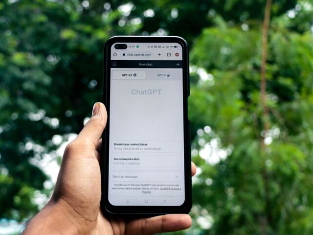 A hand holds a phone with the "ChatGPT" site on the screen.