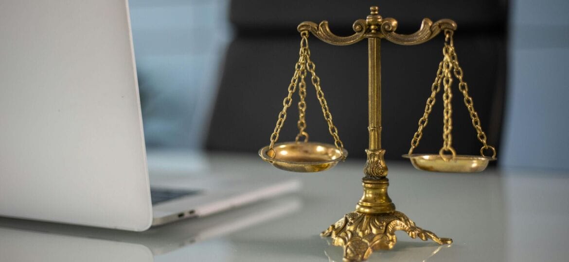 A golden scale to represent justice (Photo by KATRIN BOLOVTSOVA: https://www.pexels.com/photo/a-golden-balance-scale-beside-a-laptop-6077797/).