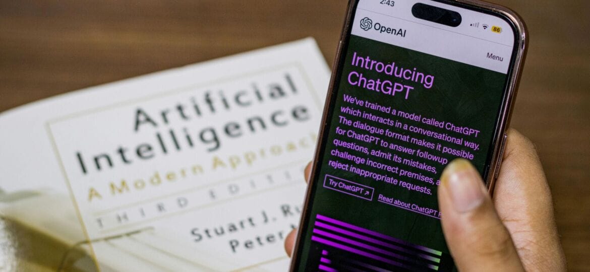 An Artificial Intelligence publication and a hand holding a phone with "ChatGPT" on the screen.
